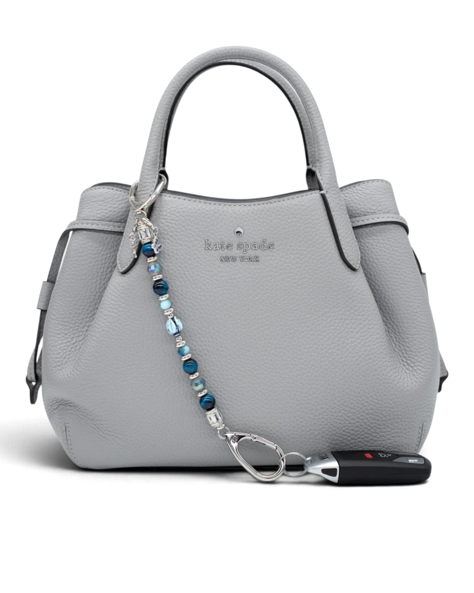 LD Keyfinder Whispering Garden accessory with blue glass tulip, tiger eye, and charms attached to a grey leather bag.
