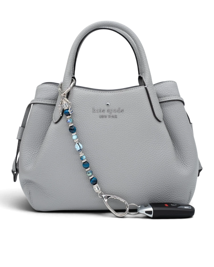 LD Keyfinder Whispering Garden accessory with blue glass tulip, tiger eye, and charms attached to a grey leather bag.