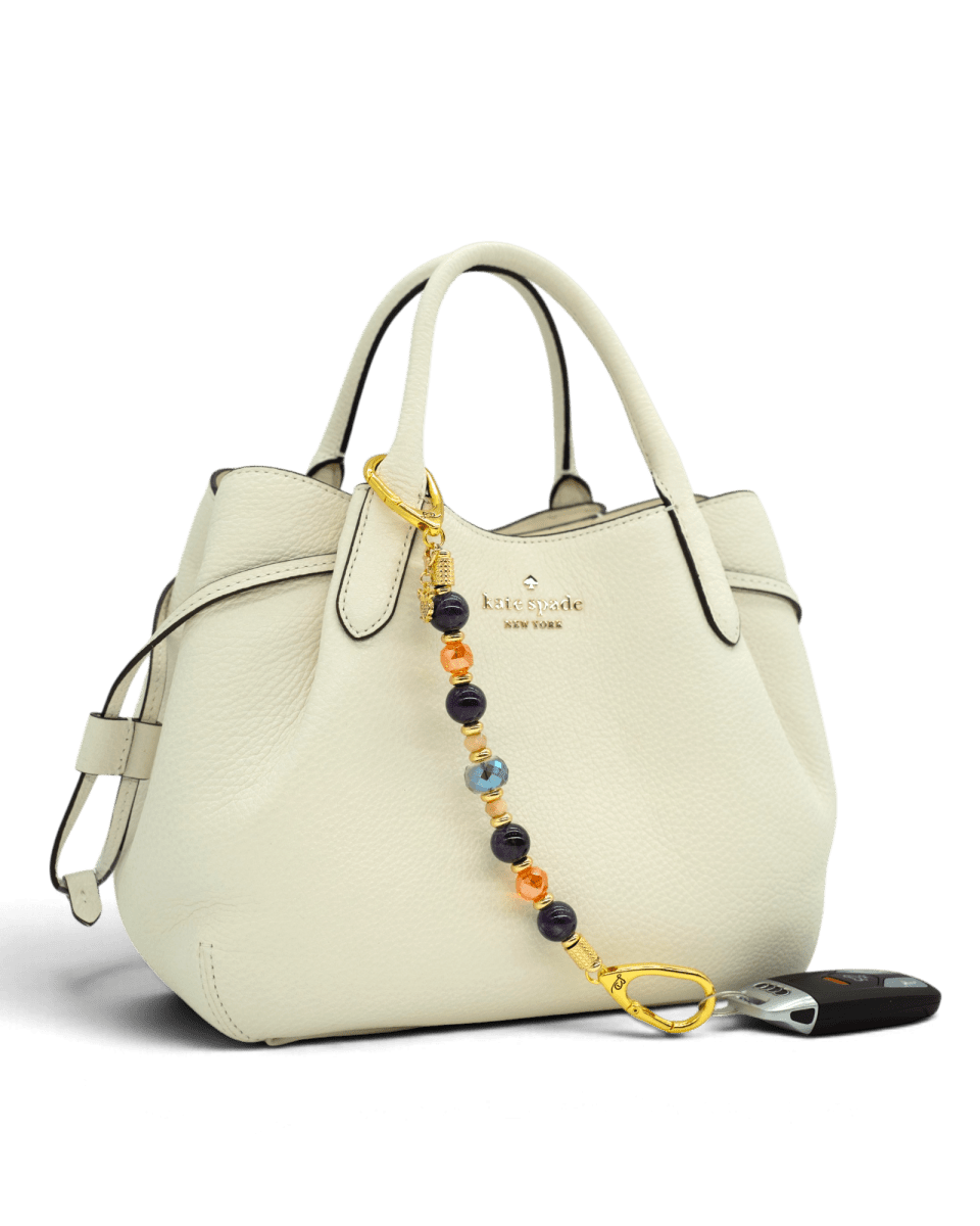 LD Keyfinder Whoo's There beaded accessory with amethyst, orange, and indigo beads and a gold owl charm on a handbag.