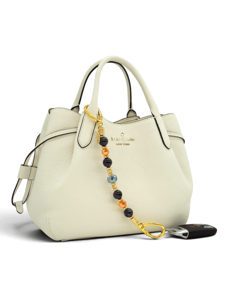 LD Keyfinder Whoo's There beaded accessory with amethyst, orange, and indigo beads and a gold owl charm on a handbag.