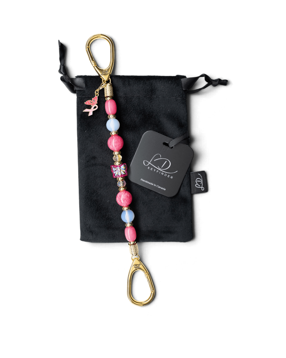 LD Keyfinder Wings of Hope beaded keychain with pink gemstones, butterfly centerpiece, and pink ribbon charm on velvet bag