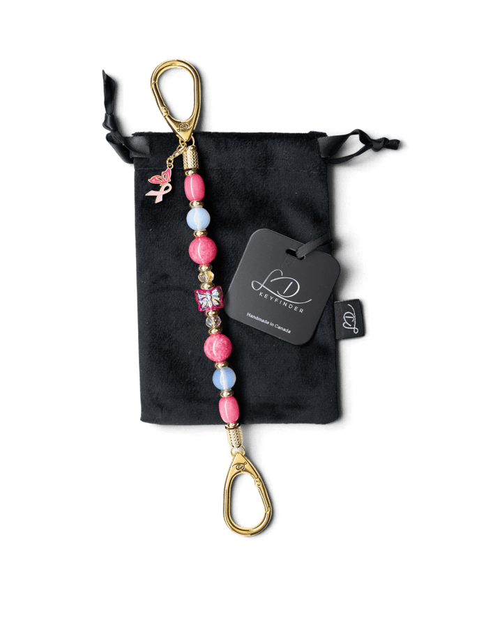 LD Keyfinder Wings of Hope beaded keychain with pink gemstones, butterfly centerpiece, and pink ribbon charm on velvet bag