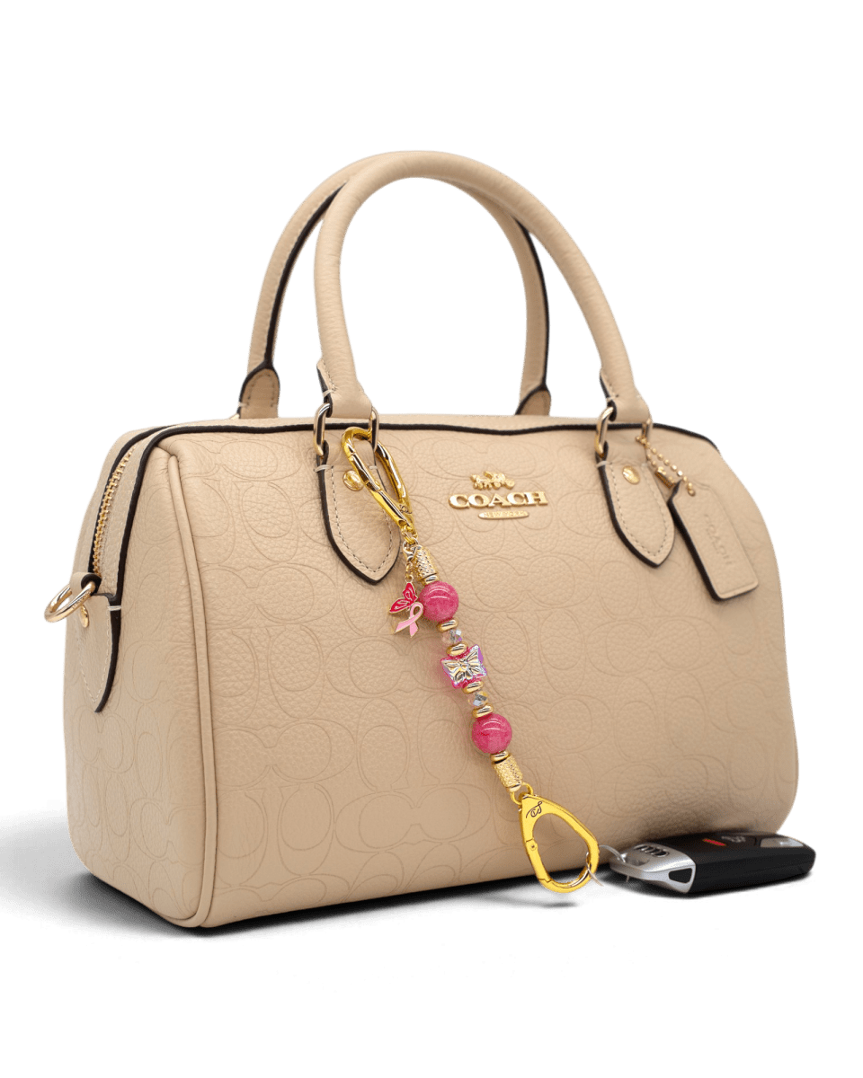 LD Keyfinder Wings of Hope Mini beaded accessory with pink jade and butterfly charm attached to a beige Coach handbag.