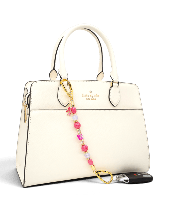 LD Keyfinder Wings of Hope pink gemstone beaded key chain with butterfly charm attached to a white handbag