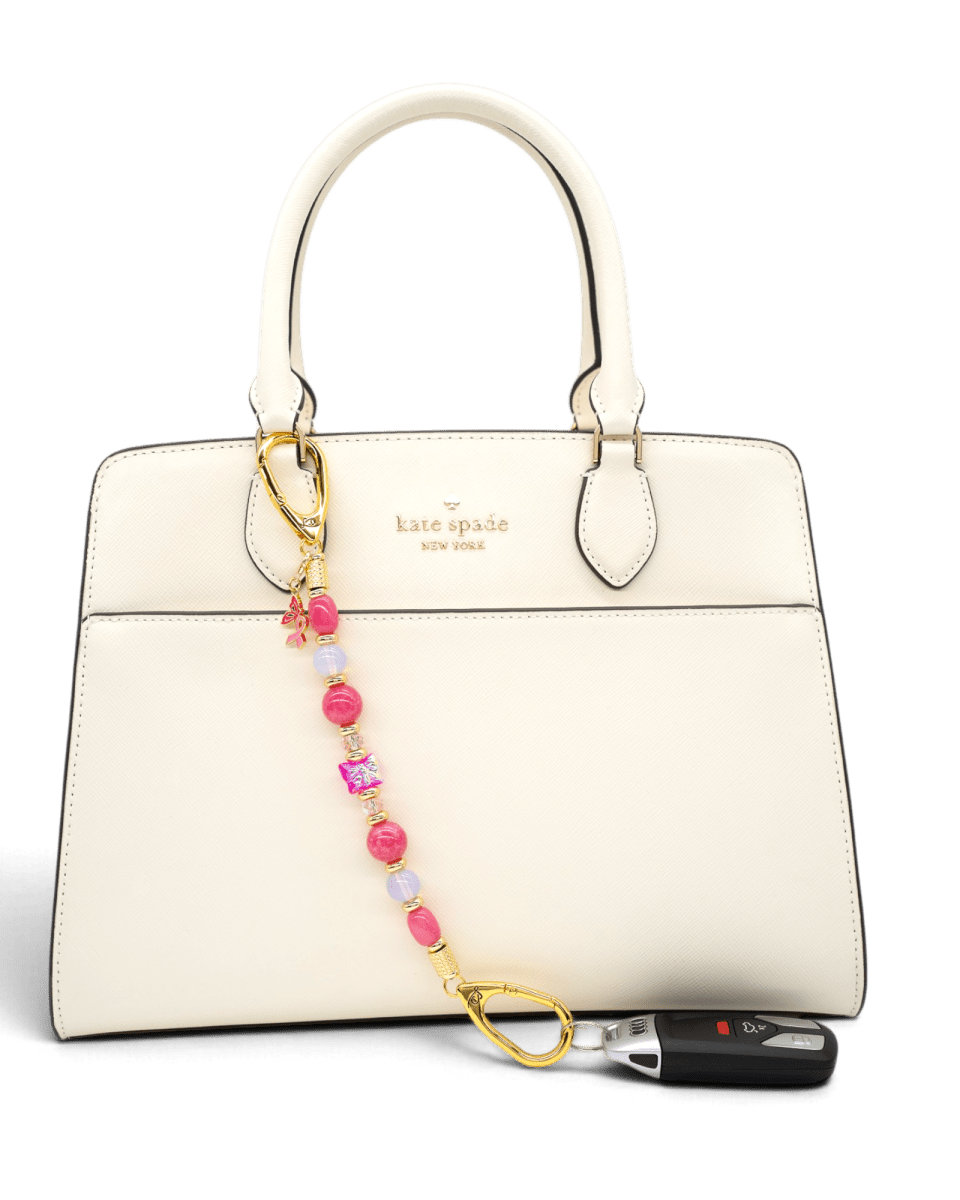 LD Keyfinder Wings of Hope beaded keychain with pink gemstones and butterfly charm attached to a cream handbag